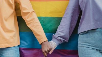 photograph of two women holding hands in front of a pride flag